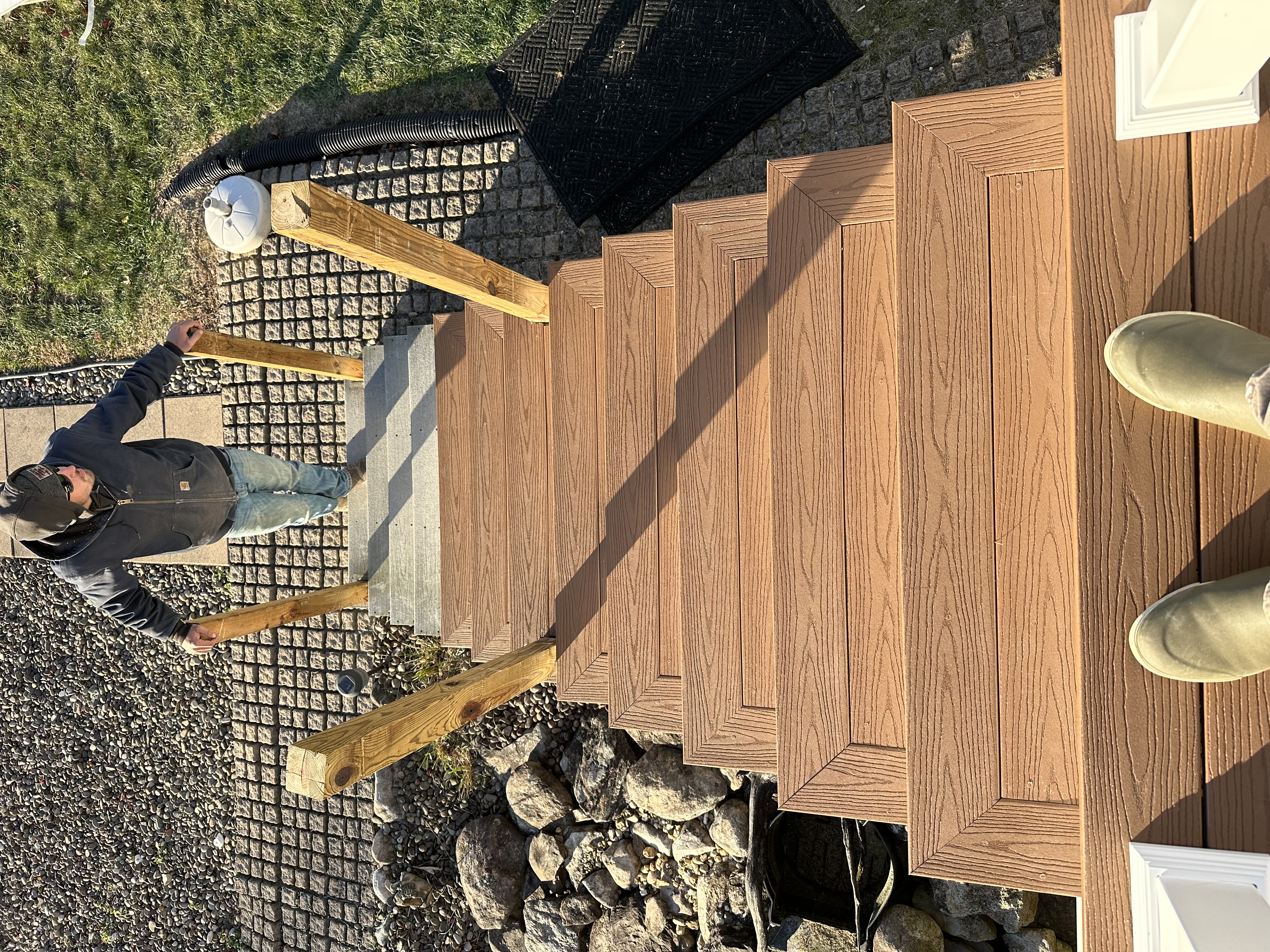 New deck stairs leading down to a stone paver patio and koi pond